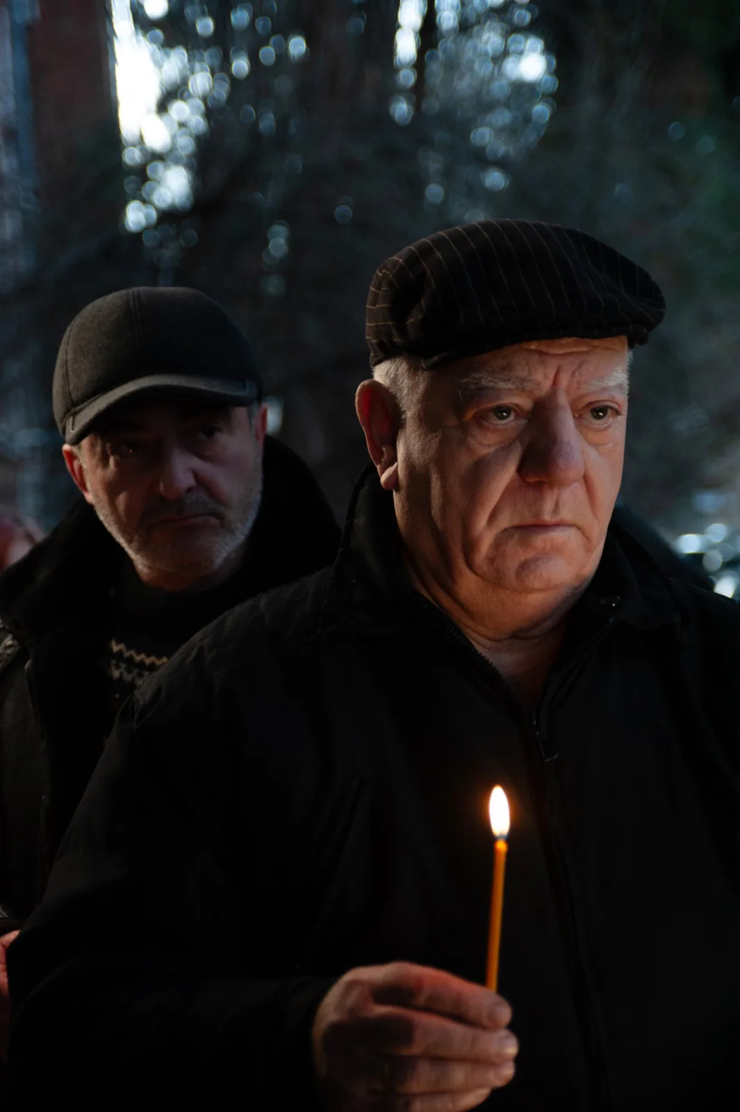 Holy Smear still: an older man holding a candle, another behind him