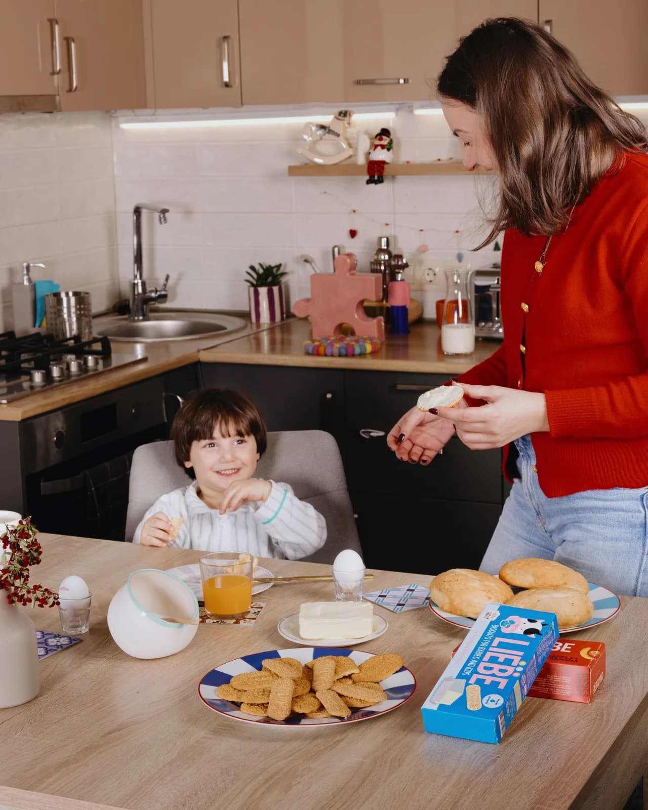 Mother buttering a Liebe biscuit for a smiling child at the breakfast table