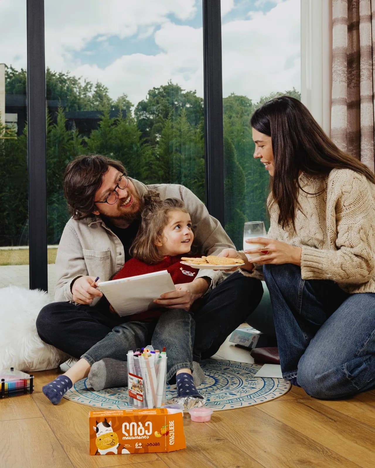 Parents and daughter on the floor by the window with a plate of Liebe biscuits and a glass of milk