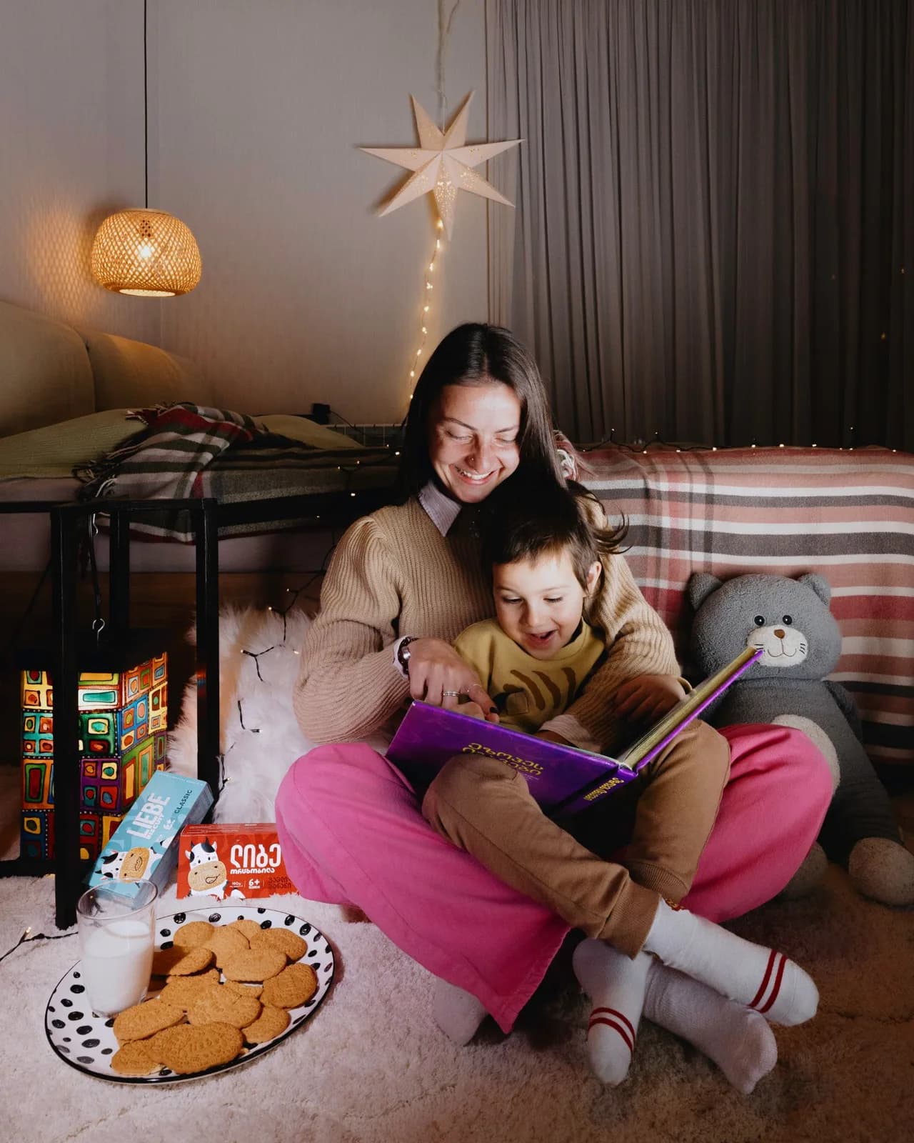 Mother and child reading a book under fairy lights, Liebe packs and biscuits beside them