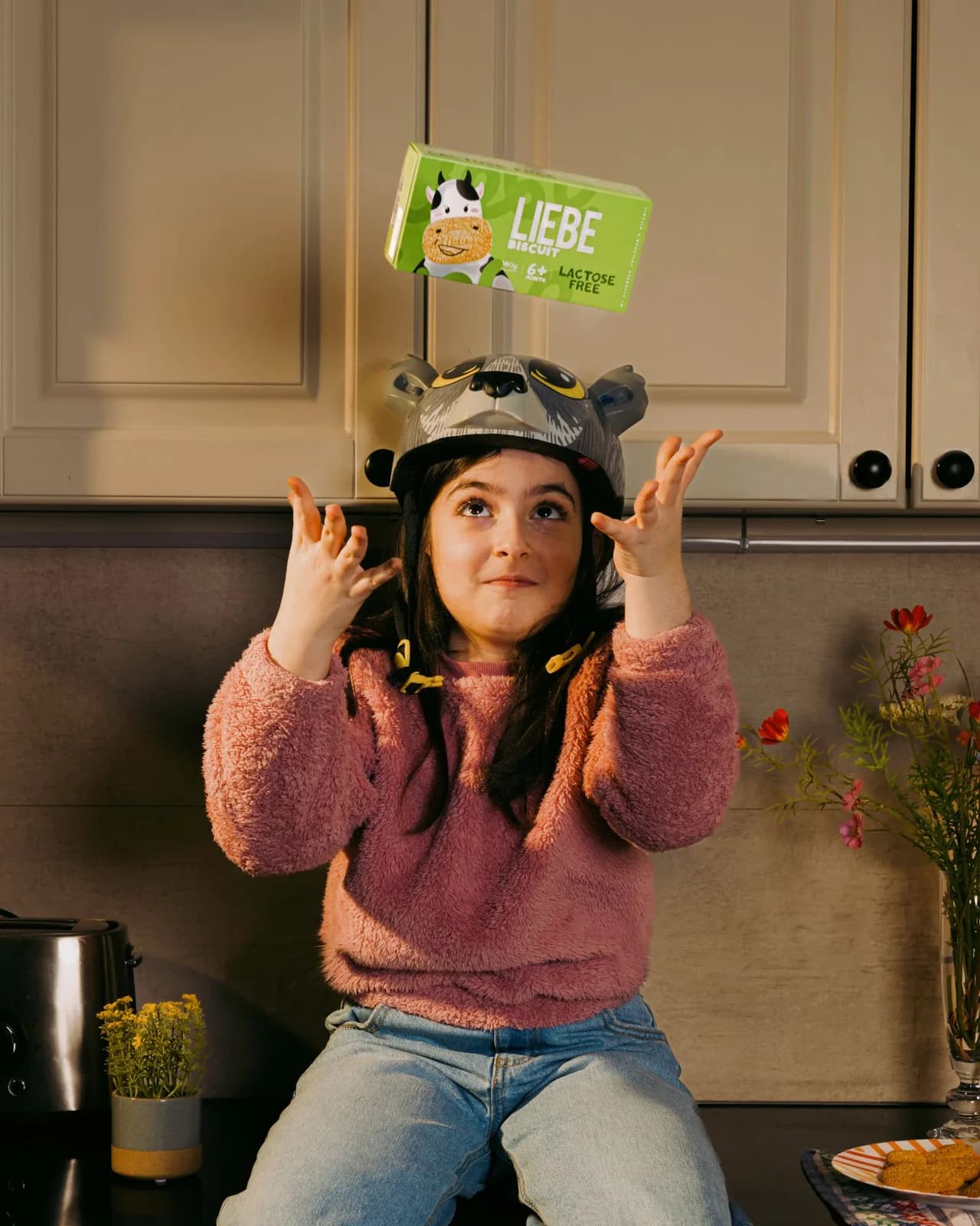 Girl in a bear helmet tossing a Liebe biscuit pack in the kitchen